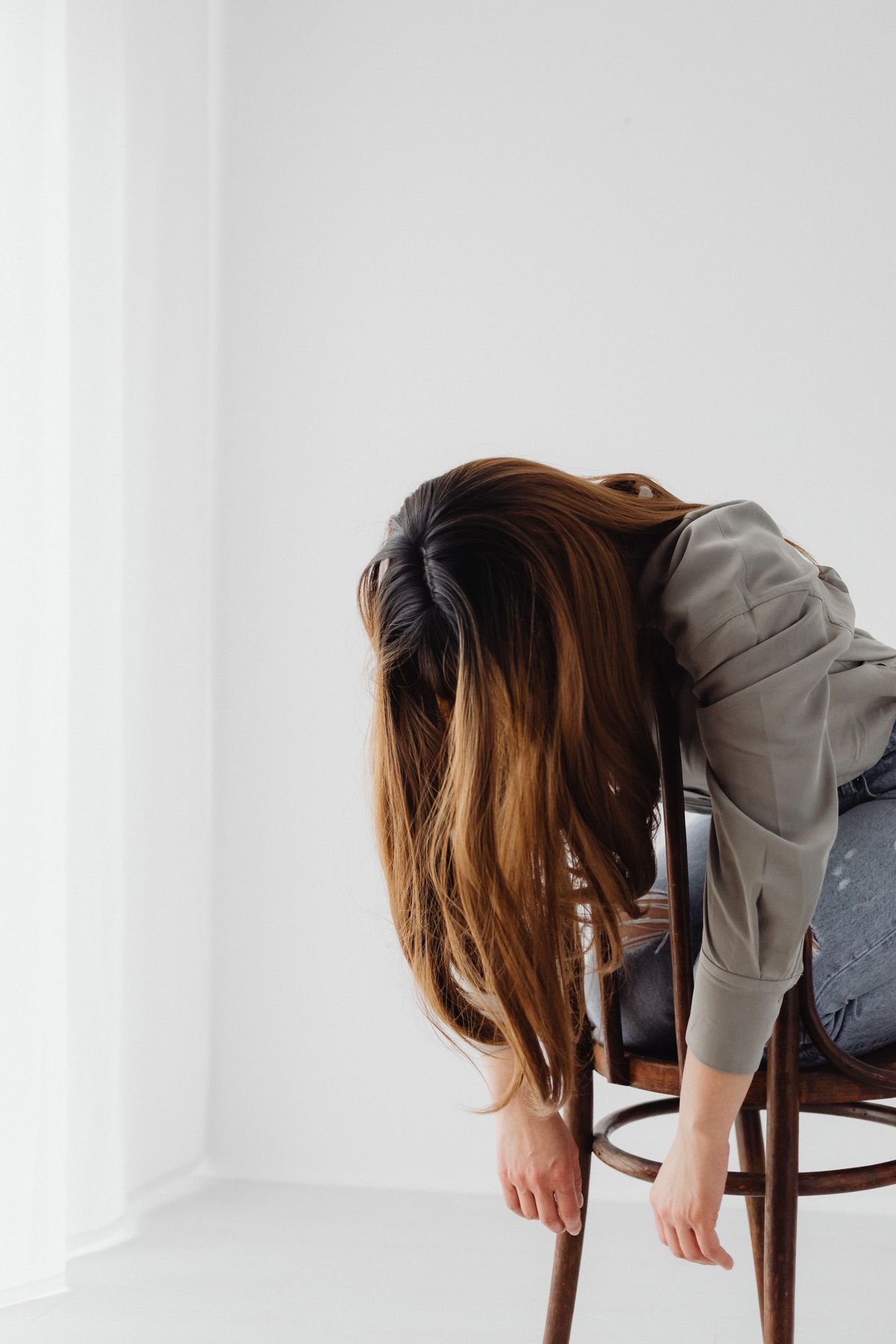 Mujer con ropa de trabajo doblada hacia delante sobre la silla, con los brazos colgando