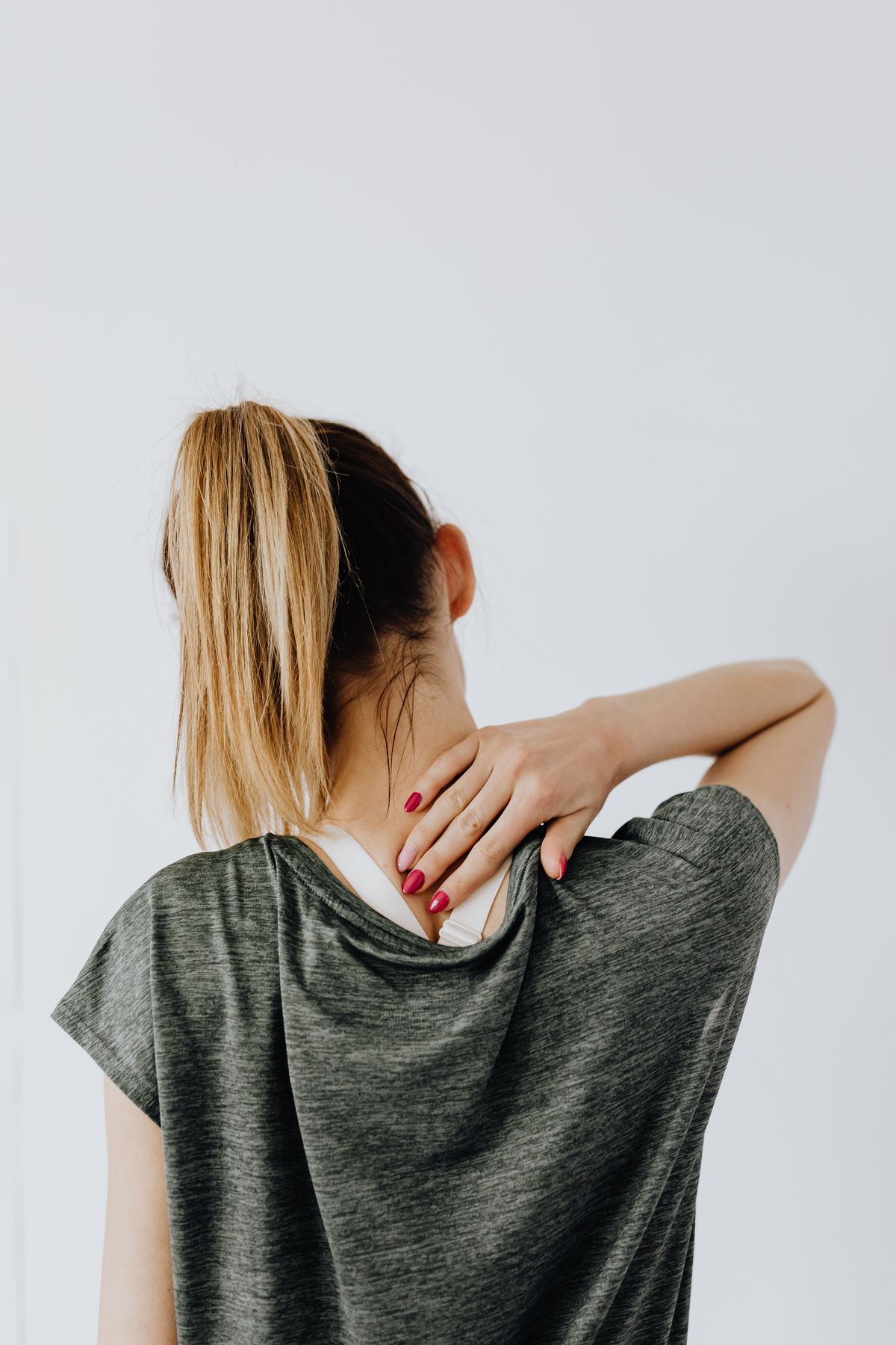 Mujer de espaldas llevándose la mano a la nuca por tensión cervical